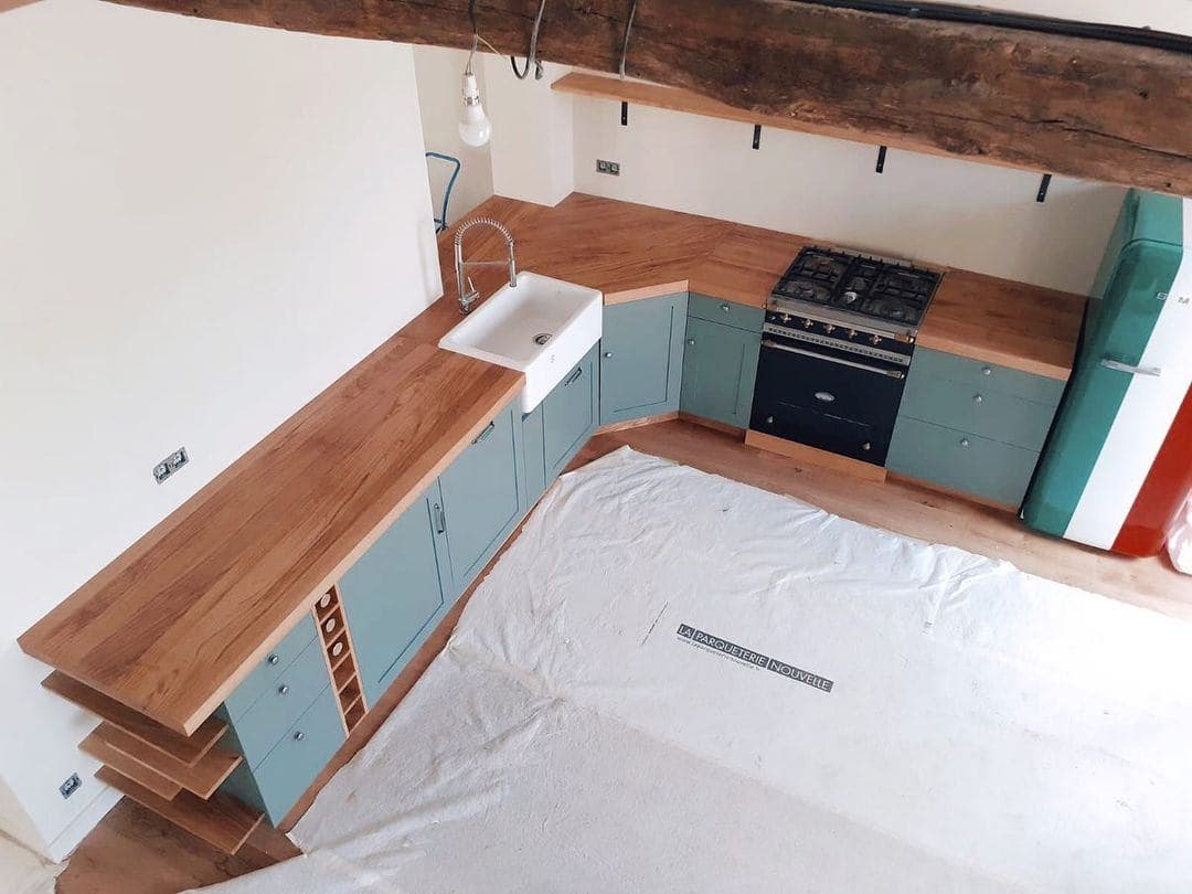 Cuisine style Mesnie du Bois, 7 tiroirs, 2 placards dont placard d'angle à 45°, lave-linge et lave-vaisselle encastré derrière leurs portes, tiroir à bouteilles et tiroir à poubelles sous l'évier, et range-bouteilles sur la gauche.