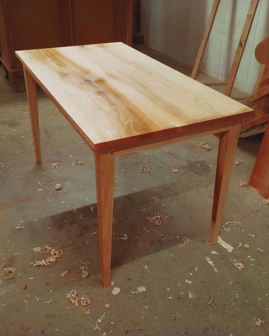 Petite table à manger en frêne massif. Pieds gainés assemblés en tenon-mortaises chevillés. Plateau verni et piétement fini à la cire d'abeille naturelle.